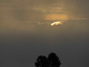 Top of sun rises above clouds at dawn
